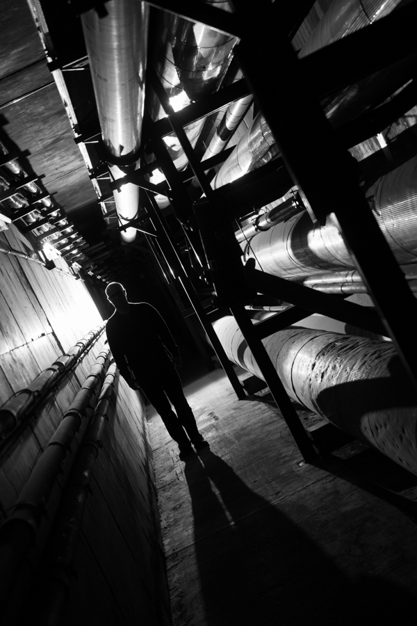 A silhouetted man walks down an errie industrial hallway.