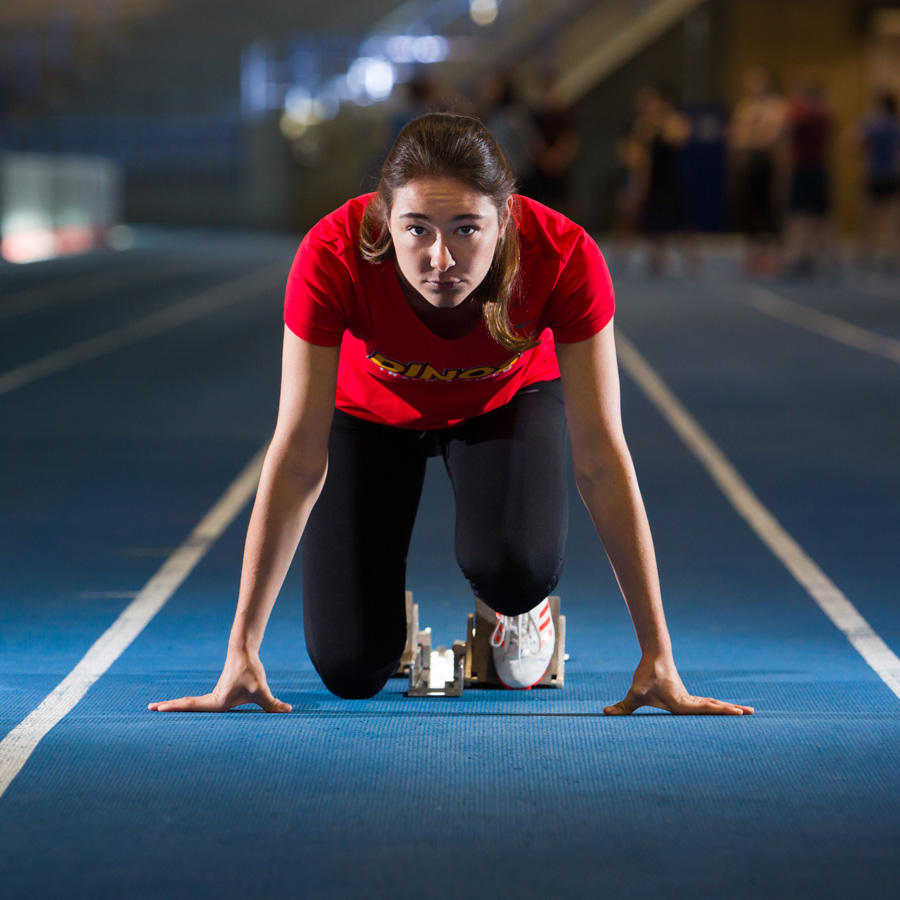 A varsity track and field athlete waits with anticipation in running block.