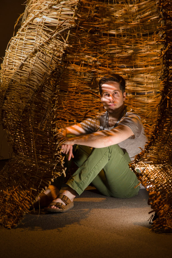 An artist sits inside his wicker bee hive art installation