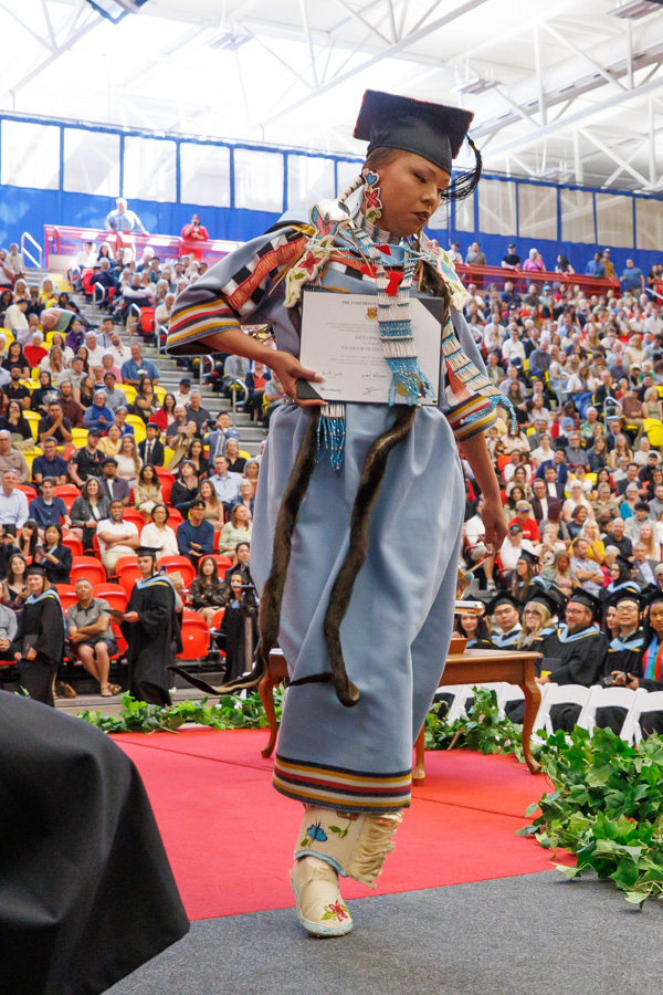 An Indigenous woman dances across the stage during graduation.