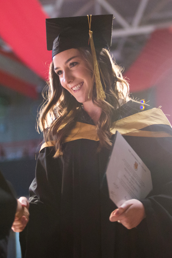 A graduate smiles and shakes hands on stage at graduation.