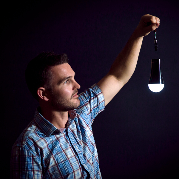 A man holds up a small solar light in a darkroom