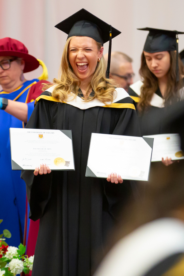 A graduate holds up two degrees
