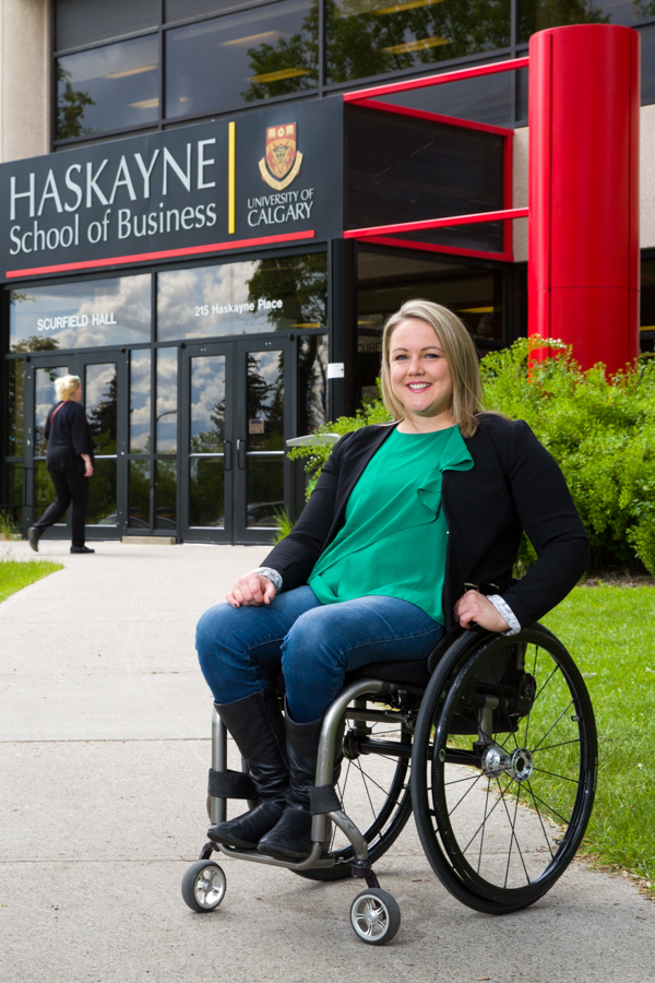 A woman in a wheelchair poses in front of a business school.