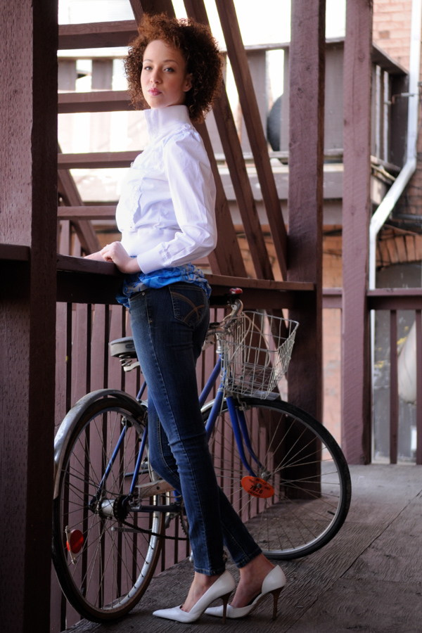 A casually dressed young woman stands be a bike.
