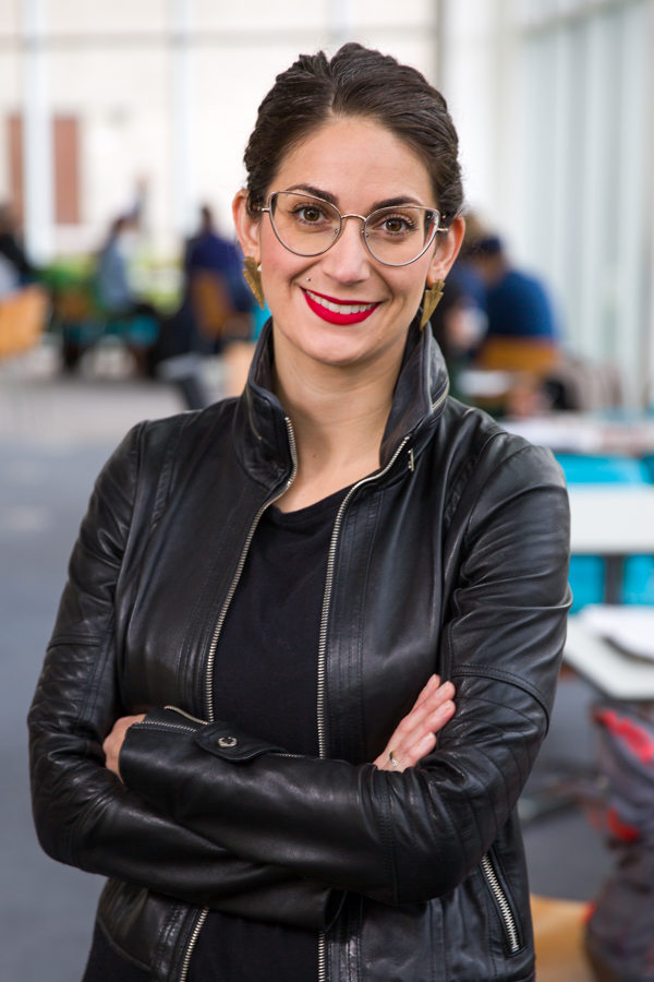 A woman in a black leather jacket crosses her arms and smiles.